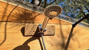 Un cabezal de ducha instalado sobre una superficie de madera, con una vista despejada del cielo y árboles al fondo.