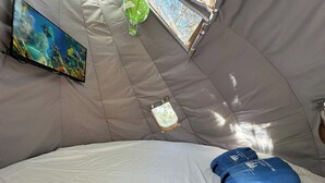 Una carpa con una cama, un televisor en la pared y una ventana pequeña.
