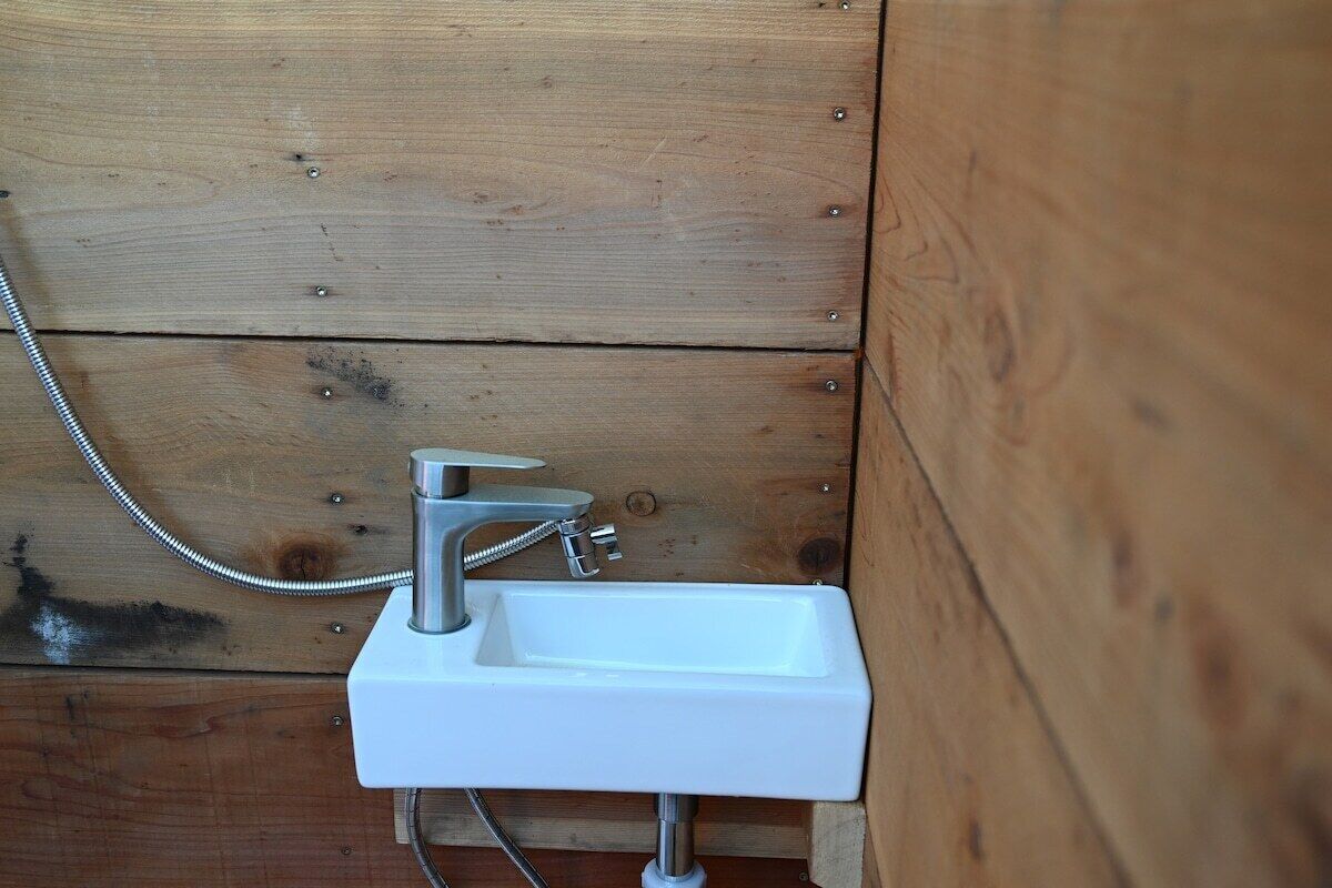 Une salle de bain avec un mur en bois, un lavabo blanc et une douchette à main.