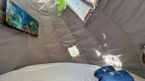 A tented room with a bed, a television mounted on the wall, and a window. - Sky Pod #2/Tree Tent 2 (Dunlap)