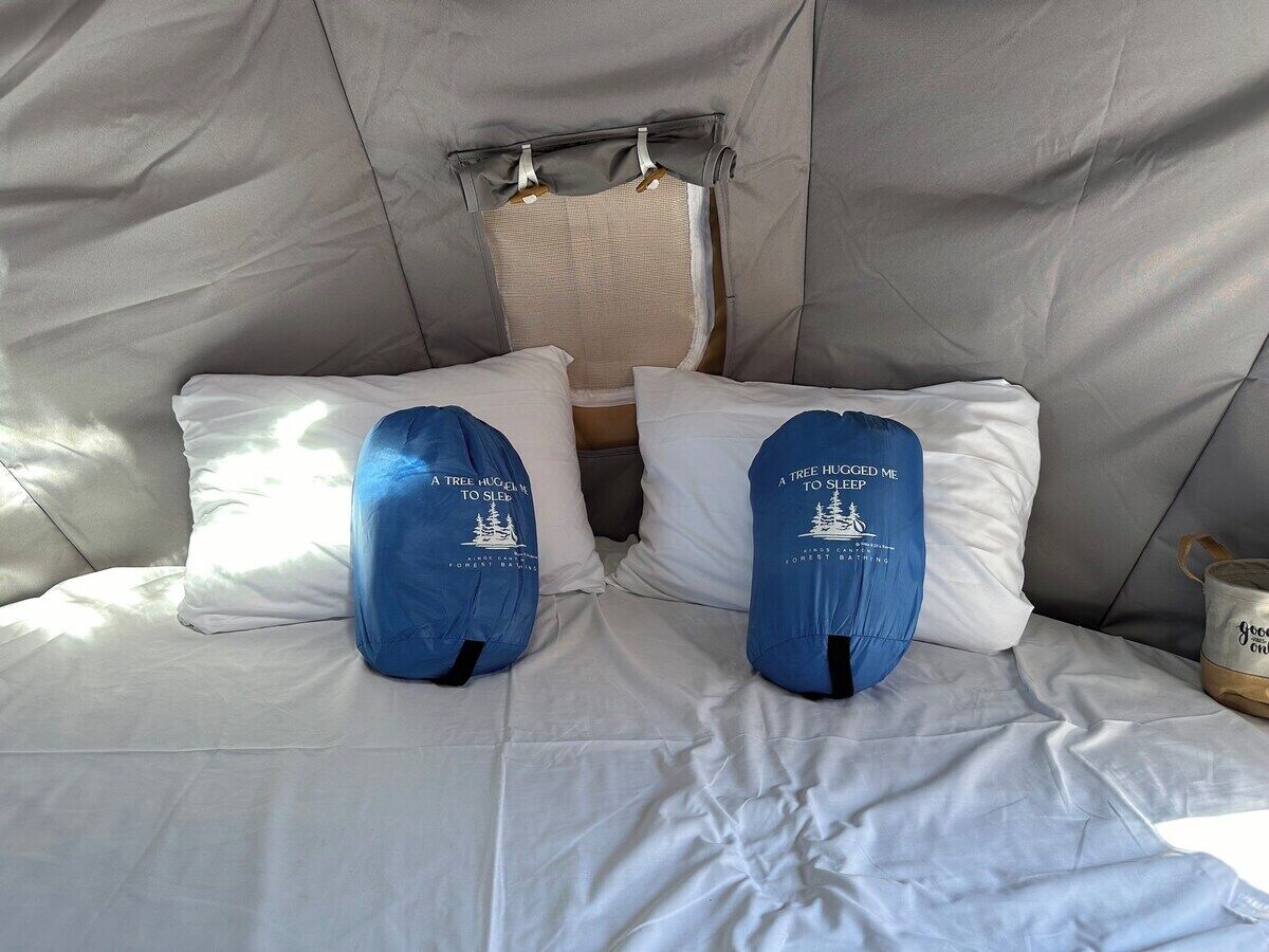 A bed with white bedding and two blue pillows with text, a window, and a small table with a cup.