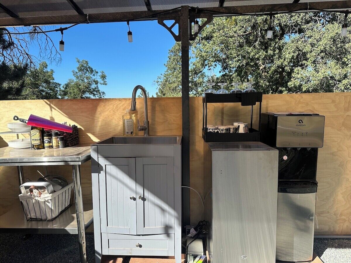 Un espace cuisine extérieur comprenant un évier, un meuble de rangement et un distributeur d’eau.
