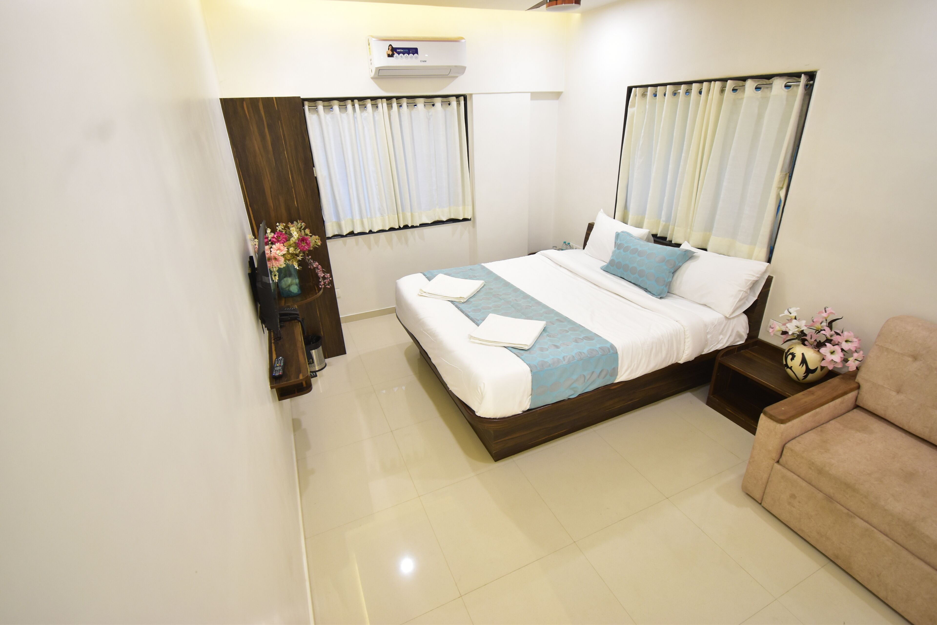 A hotel room with a bed, a sofa, a nightstand, and a window with curtains.