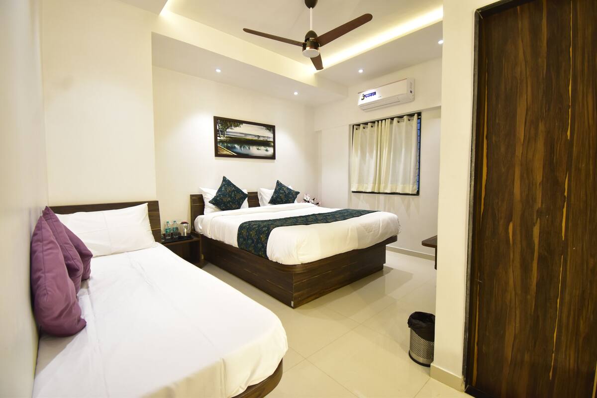 A hotel room with two beds, a ceiling fan, an air conditioning unit, a picture on the wall, and a wooden door.