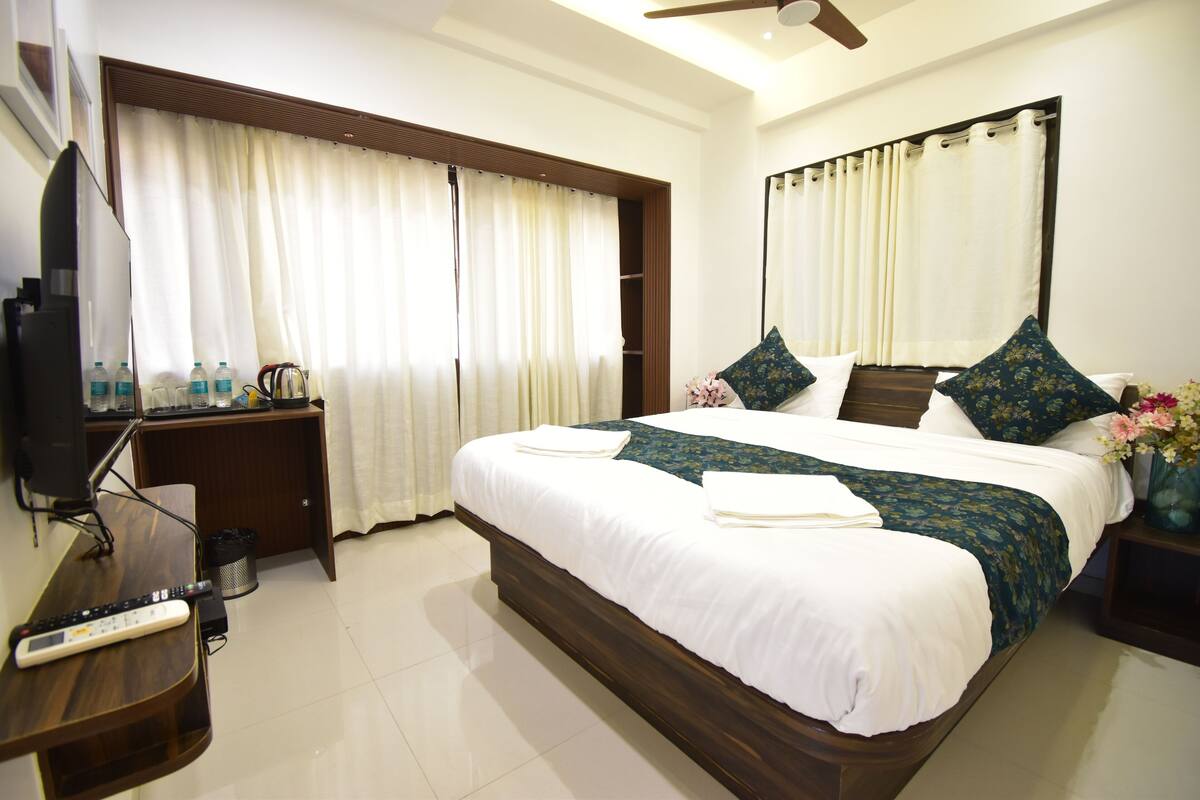 A hotel room with a large bed, a TV, a desk, and a window with curtains.