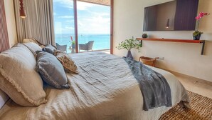 A bedroom with a large bed, a TV mounted on the wall, and a view of the ocean. - Tulum Beachfront Penthouse – Rooftop & Pool (Tulum)