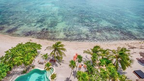 A beach with clear turquoise water, palm trees, and a pool area with lounge chairs. - Tulum Beachfront Penthouse – Rooftop & Pool (Tulum)