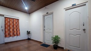 A hallway with wooden flooring, two white doors, a potted plant, and a curtain with a leaf pattern. - Misty Creek Homestay (Valparai)