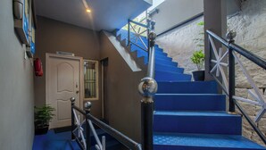 A staircase with blue steps and a metal railing, leading to a reception area with a door and a potted plant. - Misty Creek Homestay (Valparai)