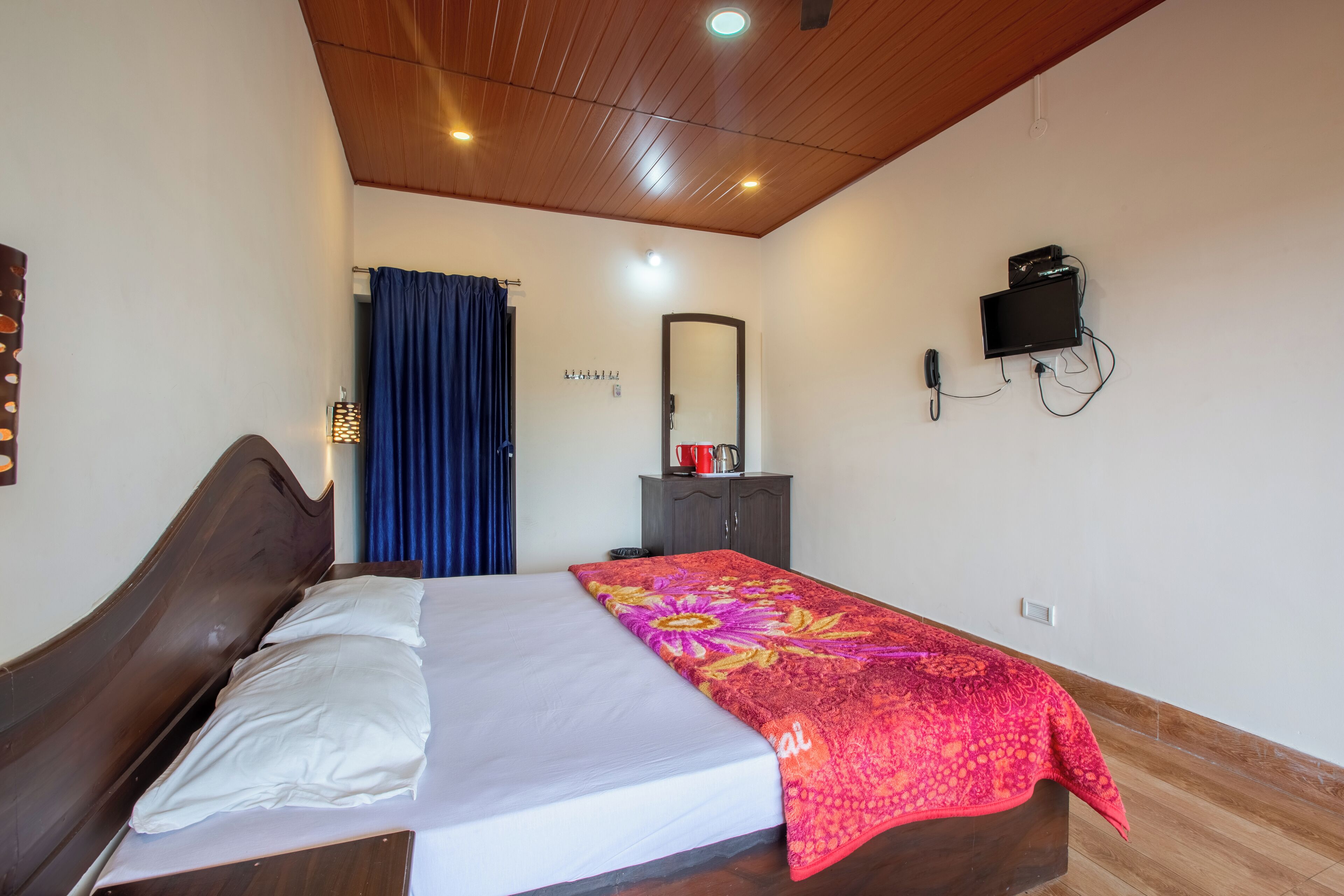 A bedroom with a bed, a dresser, a mirror, and a TV mounted on the wall.