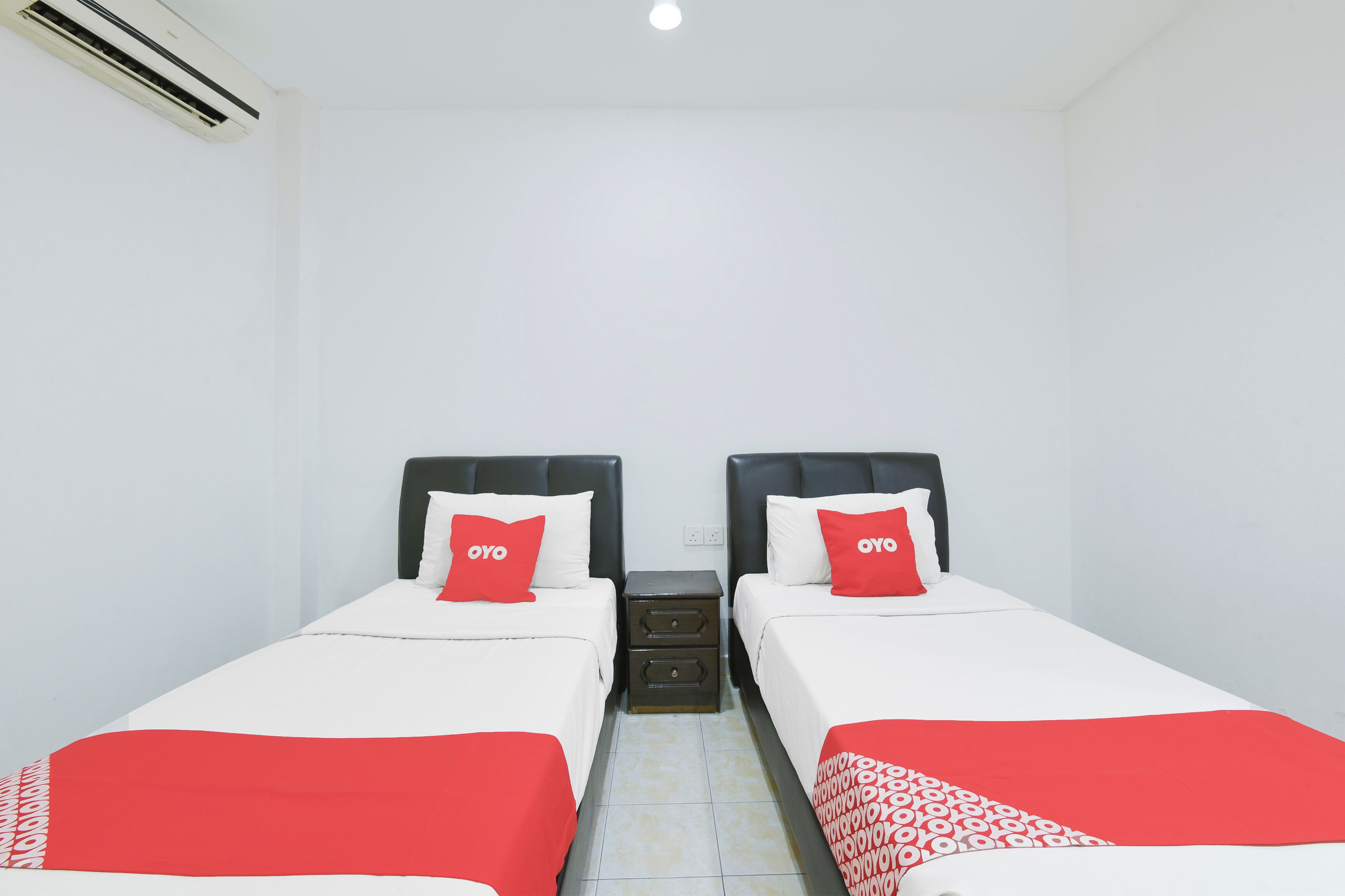 A twin room with two beds, each with a black headboard and white bedding, featuring red accents and a patterned throw.