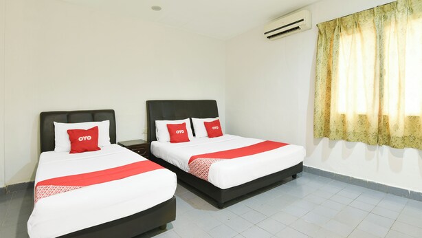 Habitación de hotel con dos camas, cada una con cabecero negro y ropa de cama blanca con detalles rojos.