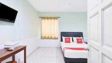 Habitación de hotel con cama, televisor montado en la pared, una mesa con silla y ventana con cortinas.