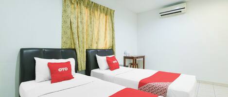 A hotel room with two beds, each with a red and white bedspread, a small table, and an air conditioning unit on the wall.