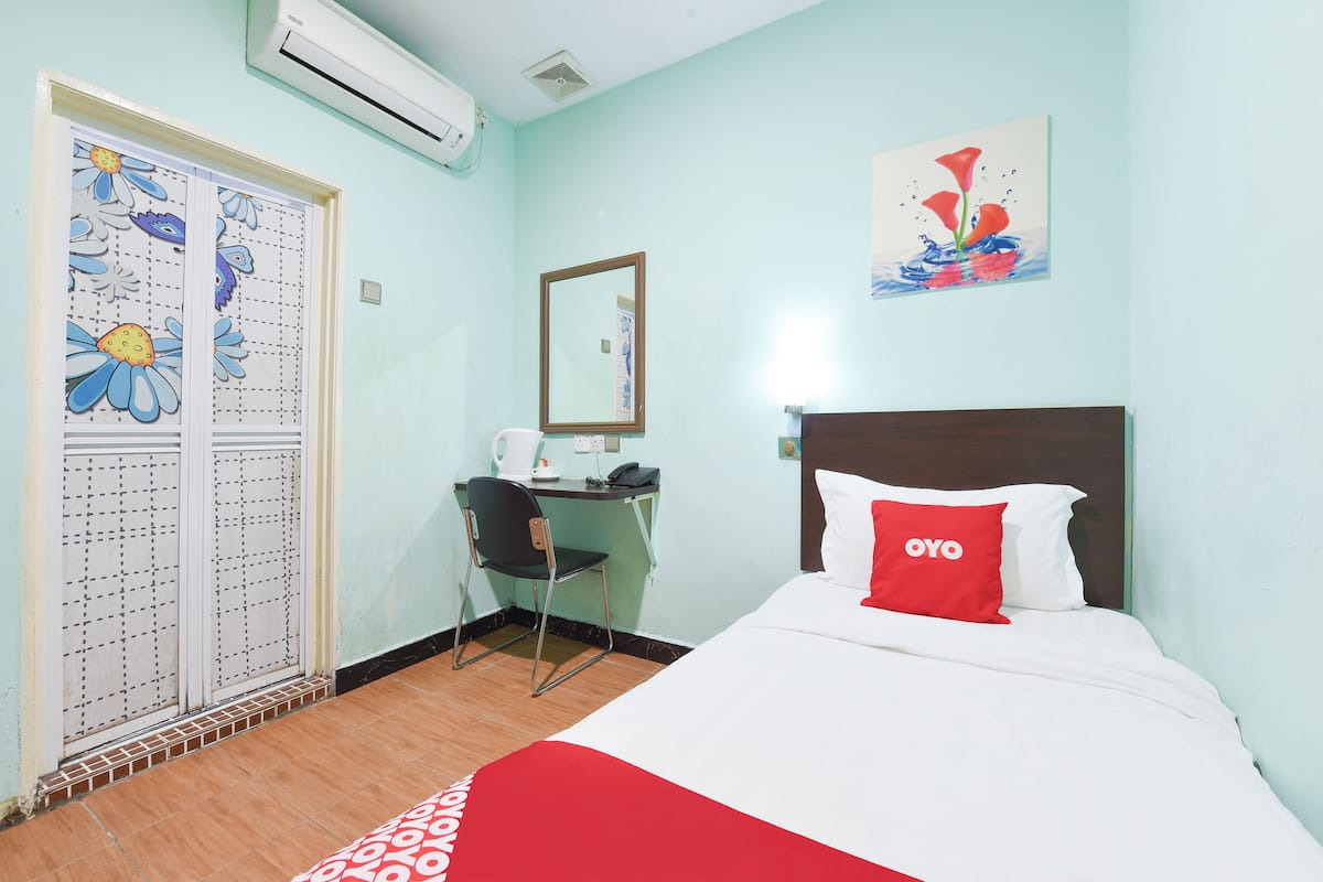 Een hotelkamer met een bed, een bureau met stoel, een spiegel en een raam met bloemmotief.