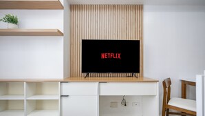 A modern living room with a flat-screen TV mounted on a wooden wall, a white cabinet with open shelves, and a wooden chair.