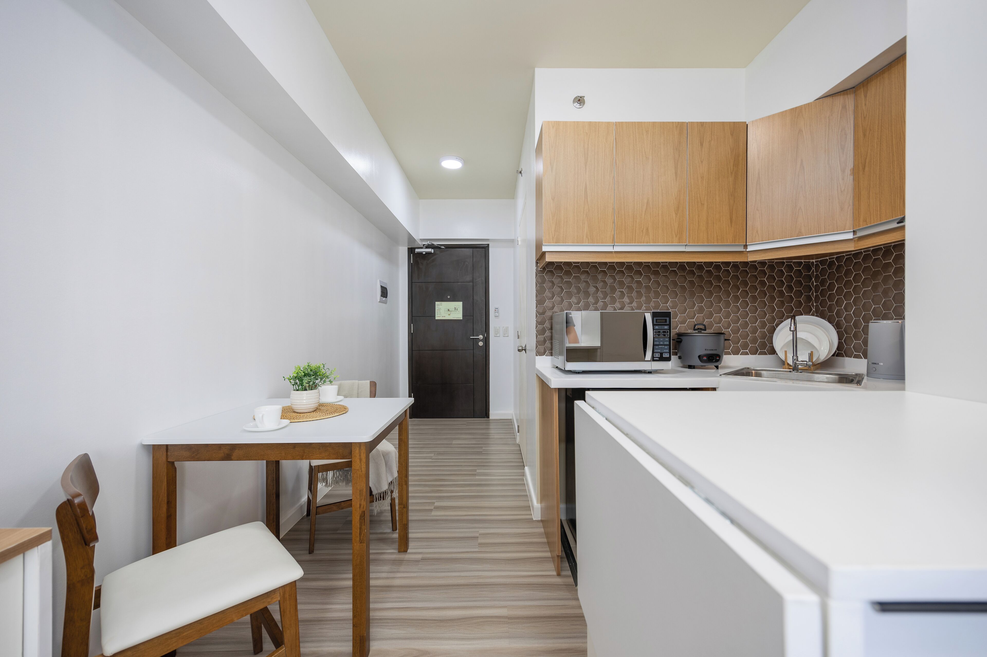 Cocina compacta con armarios de madera, microondas y un pequeño comedor con mesa y sillas.