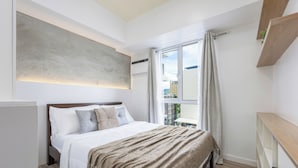 A modern bedroom with a large bed, a built-in bench, a window with curtains, and a city view.