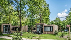 Moderni puinen mökki, jossa on lasiovet, ulkotila istuimineen ja hyvin hoidettu puutarha.