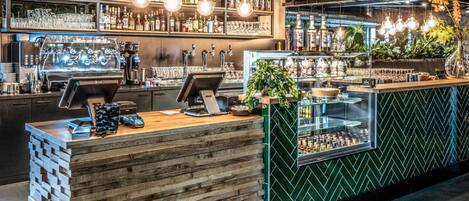 Una zona de bar con mostrador de madera, varias llaves y estantes llenos de botellas y vasos.