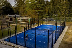 An outdoor tennis court with a net, surrounded by a fence, and trees in the background.