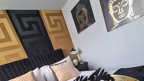 A neatly made bed with a black headboard, white and patterned pillows, and a decorative bowl of grapes and ice on the bed.
