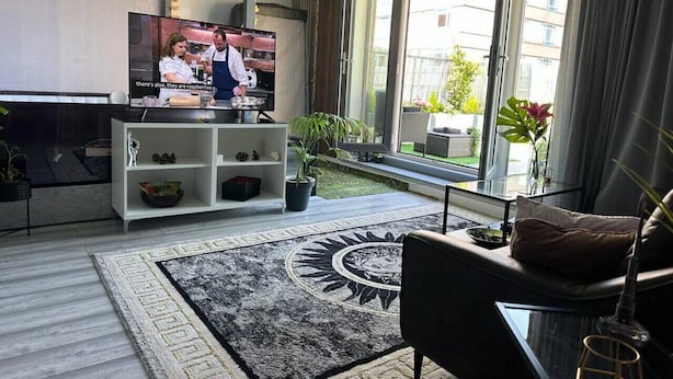A modern living room with a television, a sofa, a coffee table, and a large window with curtains.