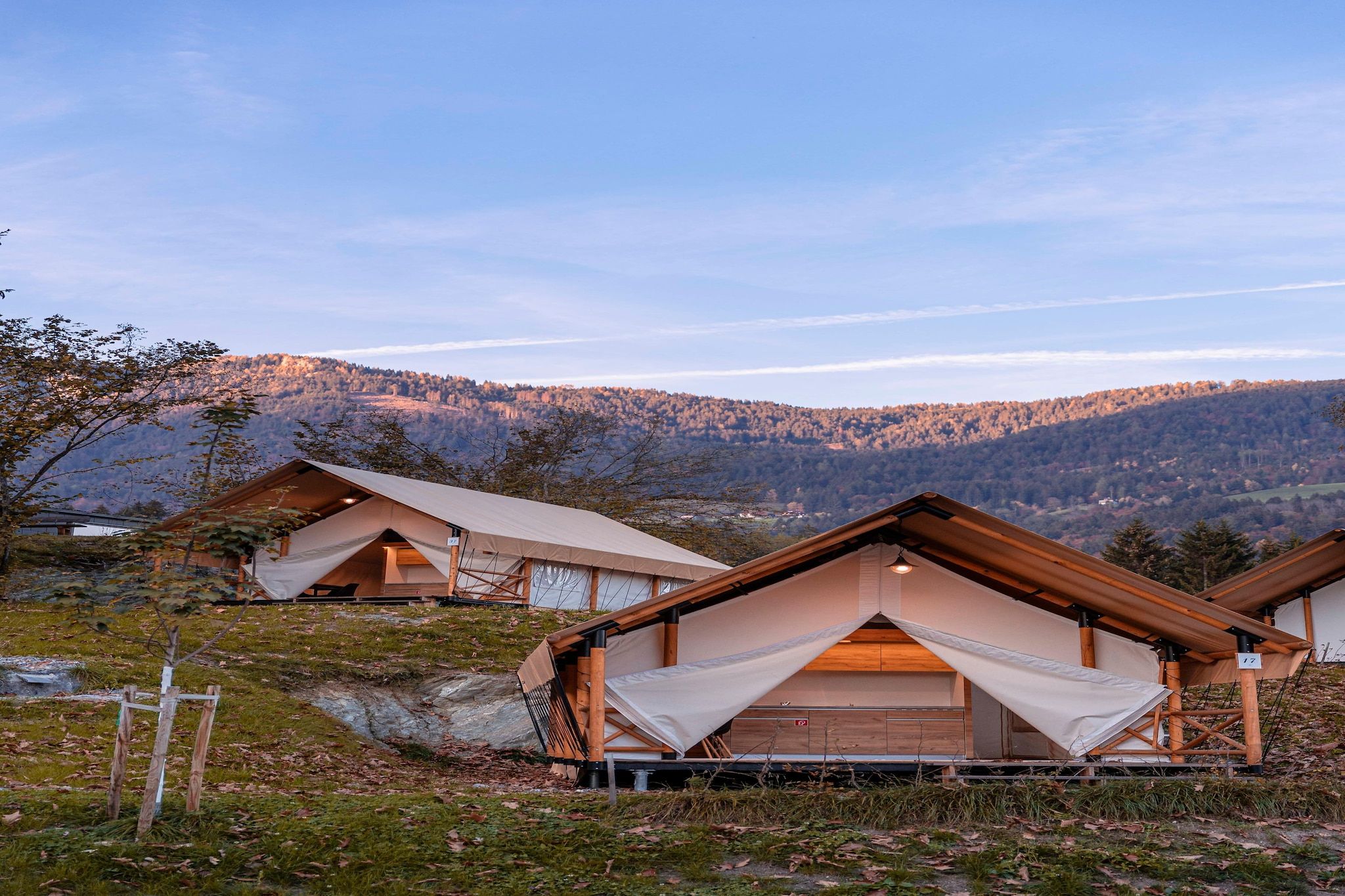 A series of wooden cabins with large windows, set against a mountainous backdrop.