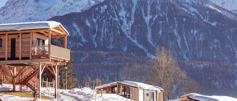Una cabaña de madera con balcón, rodeada de montañas cubiertas de nieve.