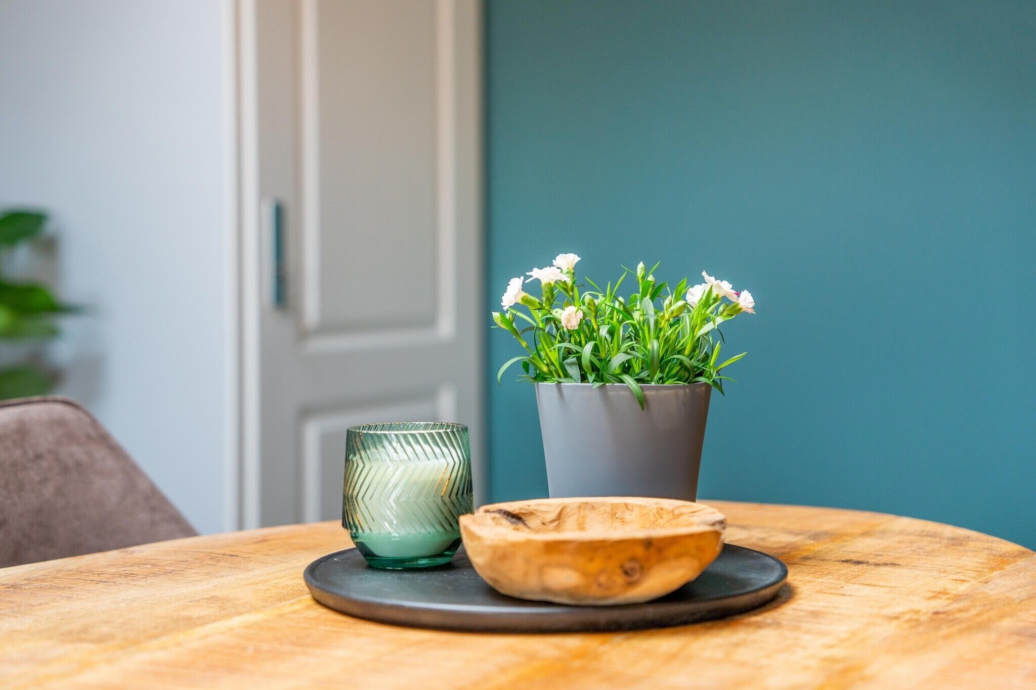 A round wooden table with a potted plant and a glass candle holder.