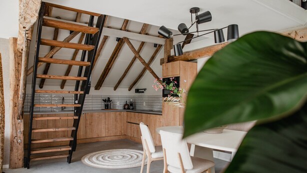 A modern kitchen with wooden beams, a white countertop, and a dining area with white chairs.