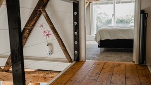 A bedroom with a wooden floor, a bed with a white cover, and a window with a view of trees.