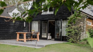 A modern house with a wooden exterior, a glass door entrance, and a small patio with a table and chairs.