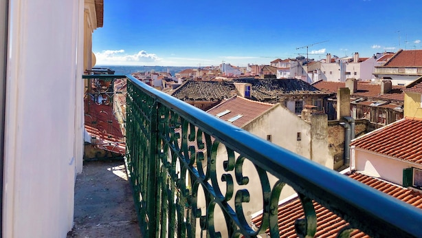 A balcony with a metal railing overlooking a cityscape with red-tiled roofs and white buildings. - Room-7lisbon Downtown Private Bedroom Wi (Lisbon)
