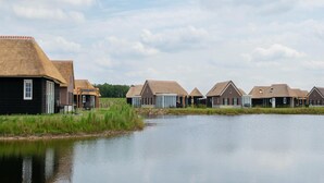 A row of thatched-roof cottages by a calm lake, with a clear sky above.