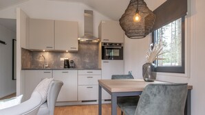 A modern kitchen with white cabinets, a built-in oven, and a dining area with a wooden table and grey chairs.