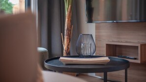A modern living room with a large flat-screen TV, a wooden coffee table, a decorative vase, and a large plant.