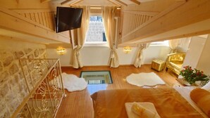 A cozy attic bedroom with a wooden ceiling, a flat-screen TV, a large bed with a fluffy white rug, and a small table with a golden lamp. - Villa madonna della Strada A5 (Dubrovnik)