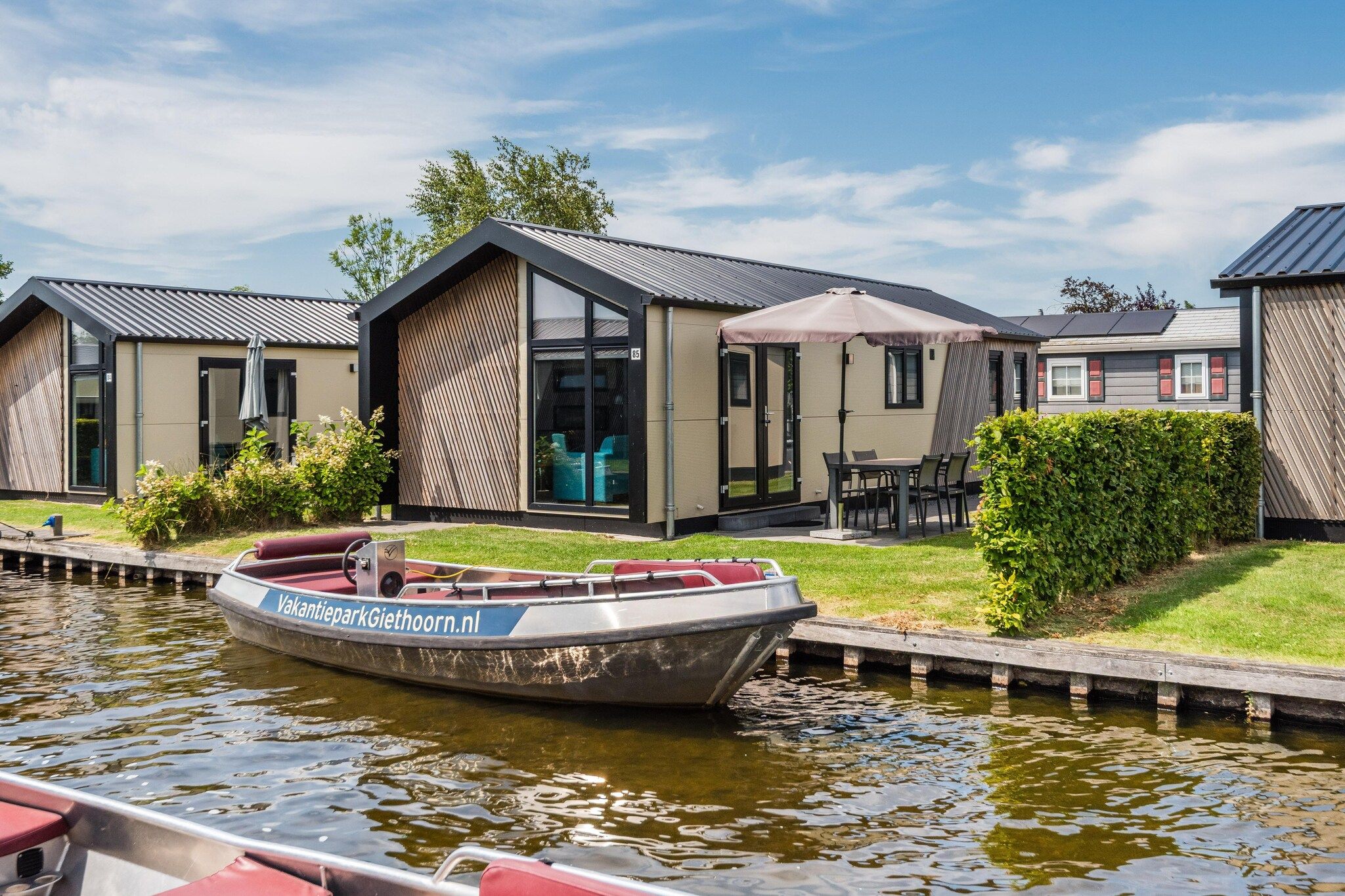 A modern houseboat with a label 'VakantieparkGiethoorn.nl' docked at a canal.