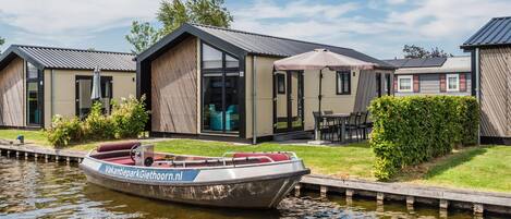 A modern houseboat with a label 'VakantieparkGiethoorn.nl' docked at a canal.