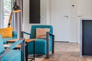 A modern living room with teal upholstered chairs, a wooden coffee table, and a black floor lamp.