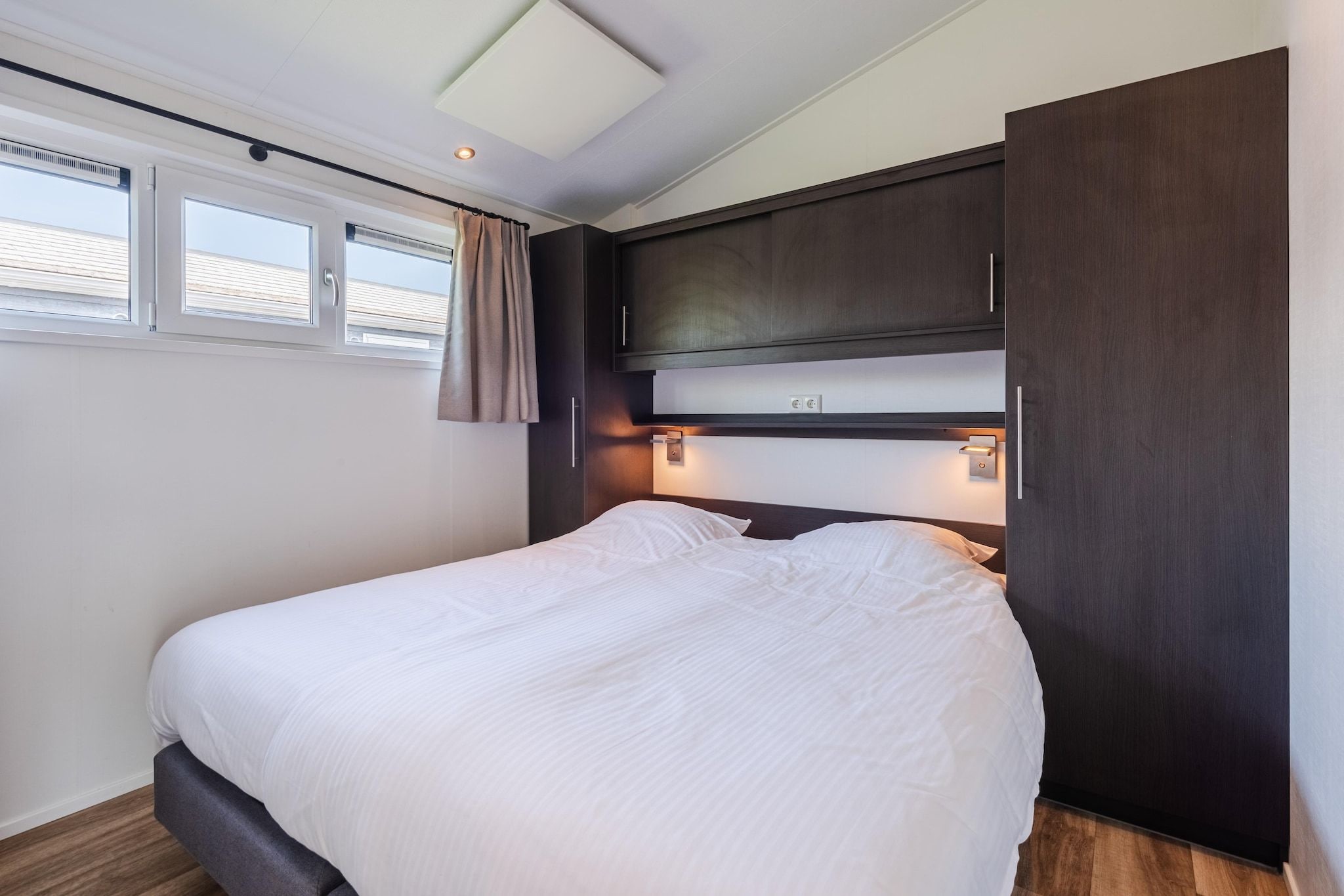 A modern bedroom with a bed, built-in cabinets, and a window with curtains.