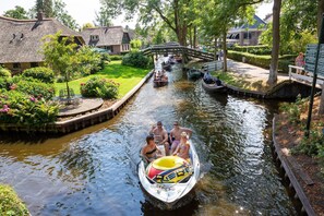 Een gracht met boten, een houten brug en gebouwen met rieten daken.