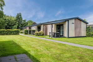 A modern caravan with a covered outdoor seating area, a paved walkway, and a well-maintained lawn.