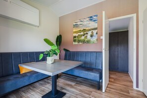 Un salon moderne avec un canapé bleu, une table sur laquelle est posée une plante, un tableau accroché au mur et une porte donnant sur une autre pièce.