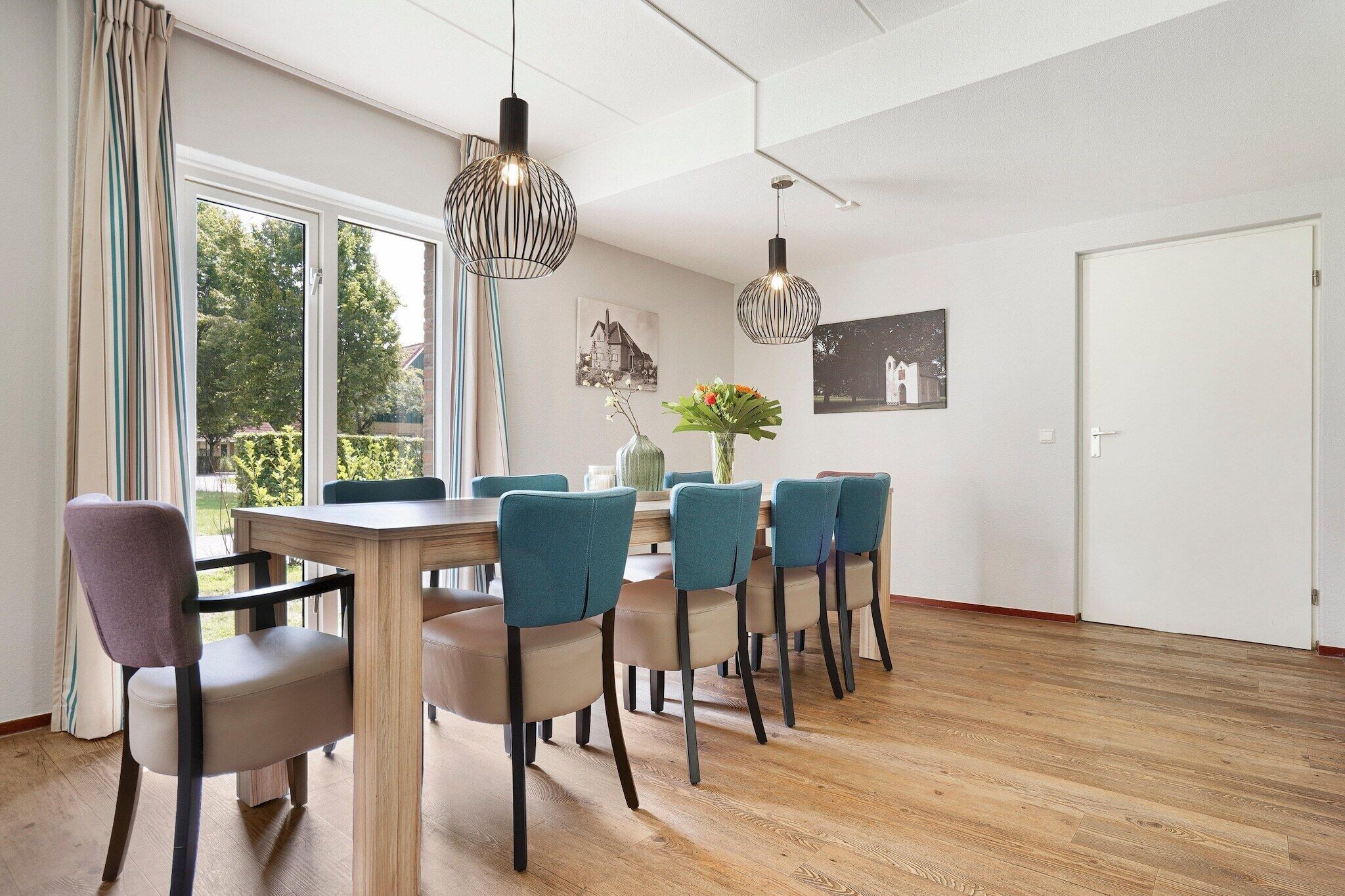Een eetruimte met een houten tafel en stoelen, hanglampen en kunstwerken aan de muren.