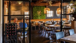 Un restaurant au décor rustique, avec des tables et des chaises en bois, un mur végétal orné du logo de l’établissement et des lampes en osier suspendues au plafond.