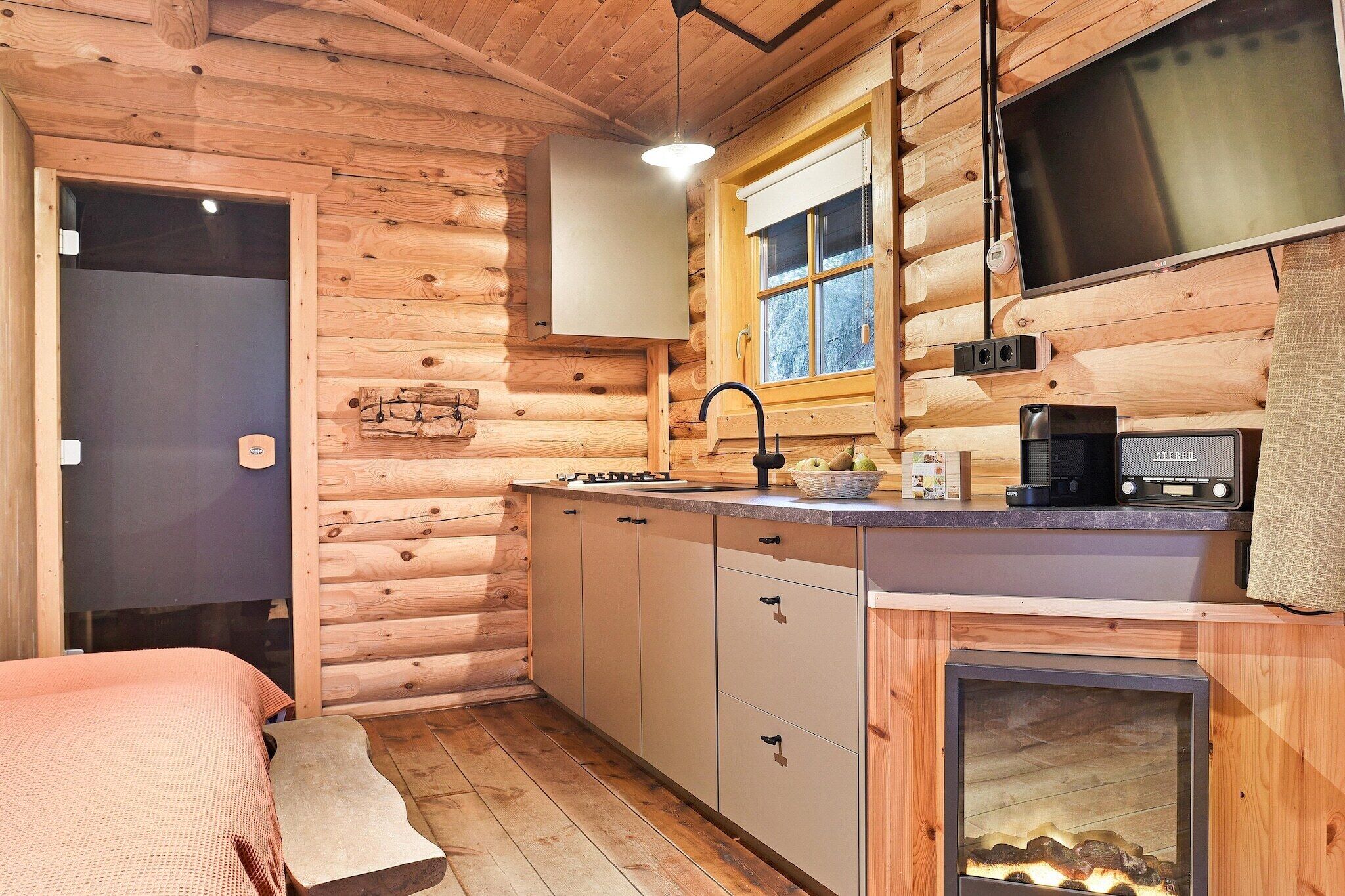 A compact log cabin with a kitchenette, a bed, and a fireplace.