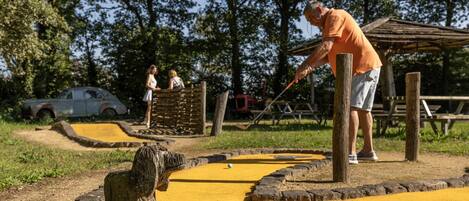 A man playing shuffleboard in an outdoor setting with a wooden structure and a yellow playing surface.
