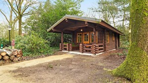 Un chalet rustique doté d’un porche, entouré d’arbres et bordé d’un sentier de terre.